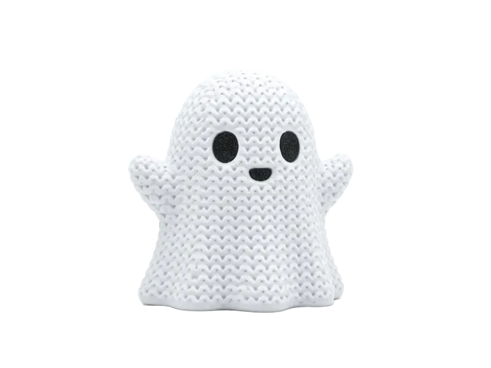 A white knitted ghost figurine with black embroidered eyes and a small black smile, standing against a seamless light gray background.